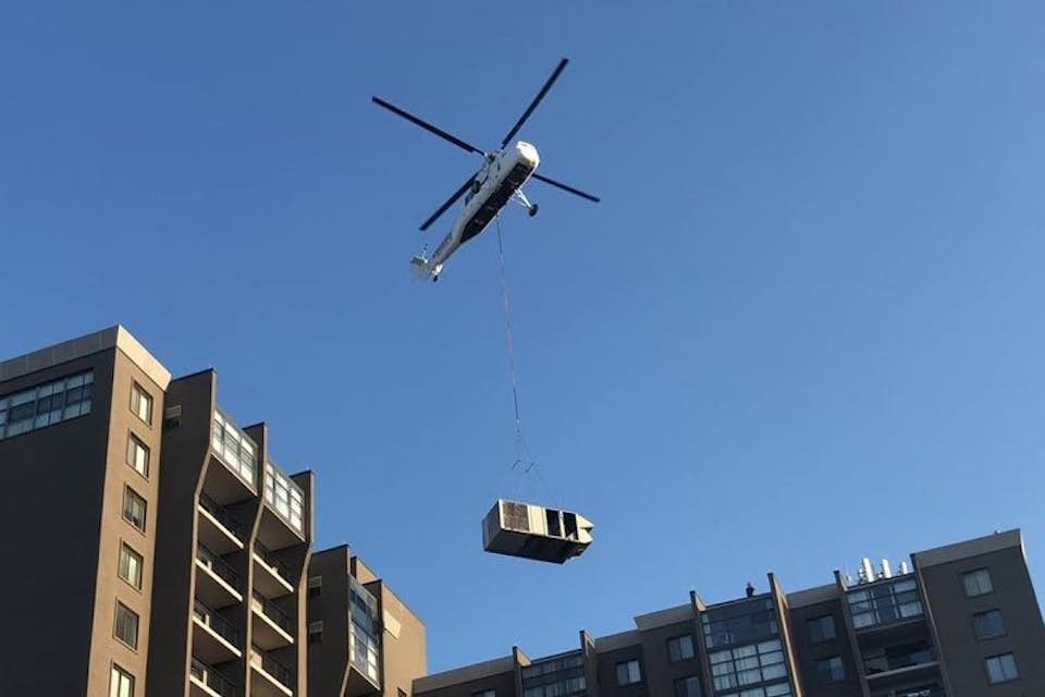 helicopter lifts HVAC next to a building