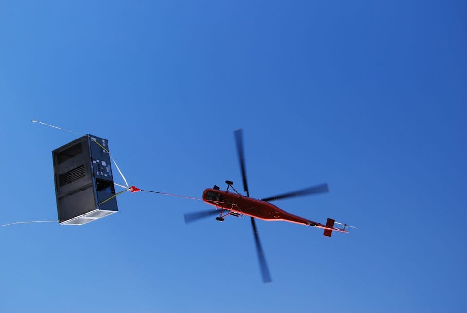 helicopter lifts hvac unit against blue sky