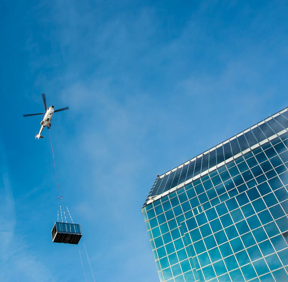 Helicopter lifts large load next to city building
